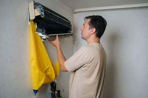 Side view of technician disassembling and repairing wall-mounted air conditioner Stockfoto's