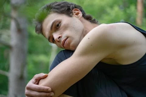 Side view of thoughtful man looking away while hugging knees in forest Stock Photos