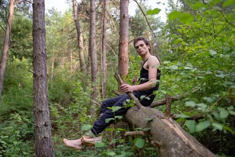 Side view of thoughtful man sitting on log against trees in forest Stock Photos