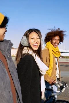 Side view of three multiethnic friends walking outdoors in a sunny day smiling Stock Photos