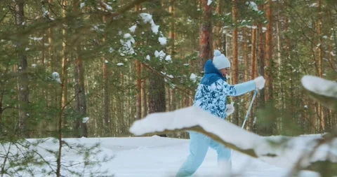 Side view through the trees of a retired woman who is skiing through the forest Stock Footage 275820499