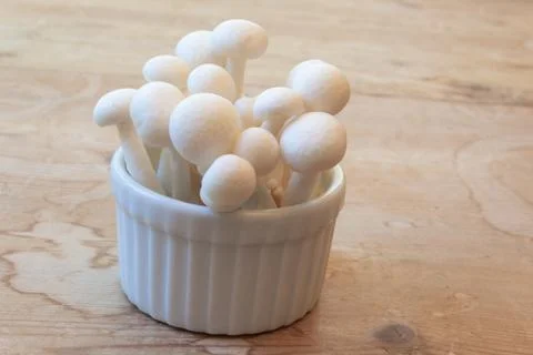 Side view of tiny ceramic dish of white mushrooms on old wood table Stock Photos