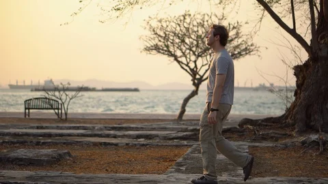 Side View Tracking Shot of Man Walking in Nature Outdoors With Ocean and Sunset Stock Footage 126259791