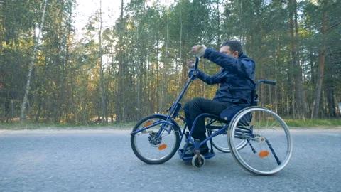 Side view of a training wheelchair getting moved by a disabled person with his Stock Footage 90914389