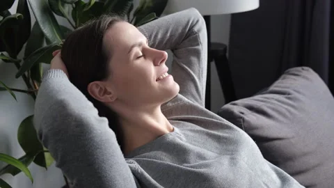 Side view of tranquil smiling pretty woman relaxing on sofa in living room Stock Footage 221685636