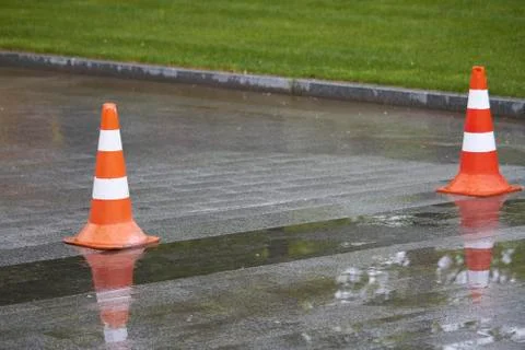 Side view of two bright orange-white warning cones on brick pavement, traffic Stock Photos