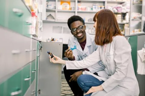 Side view of two dedicated pharmacists, African man and Caucasian woman, look Фото