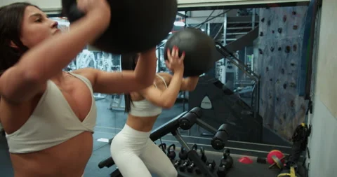 Side view of two girls in white tracksuits doing squats and throwing a sports Stock Footage 306228597