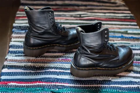 Side view of two robust, black ankle leather boots on a colorful rug Stock Photos