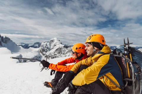 Side view of two smiling hikers in winter hiking gear sitting in the snow, high Stock Photos