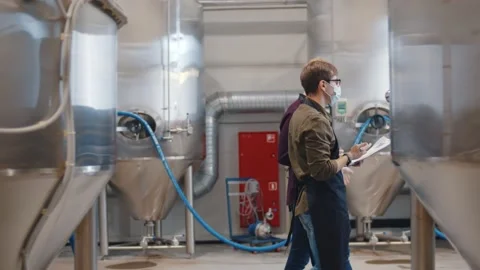 Side view of two specialists in safety mask inspecting beer factory Stock Footage 144530701