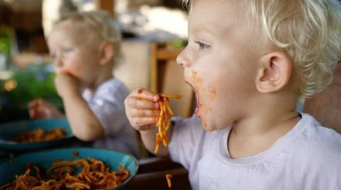 Side view of two white babies learning to feed themselves with plant based pasta Stock Photos
