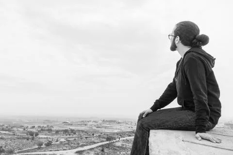 Side view unidentified young man in casual clothes and glasses sits on the hi Stock Photos