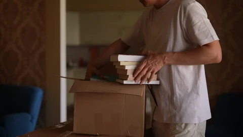 Side view of unrecognizable man packing books into cardboard box, preparing for Stock Footage 292696813