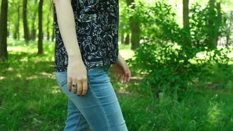 Side view of an unrecognizable womans torso and legs walking through a lush 스톡 동영상 330061437