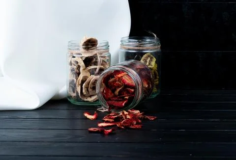 Side view of various dried fruit slices in glass jars strawberry banana and.. Stock Photos