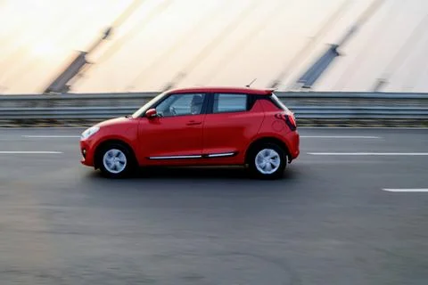 Side view of a vibrant red hatchback driving fast on a city highway bridge Stock Photos