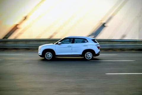 Side view of a vibrant red hatchback driving fast on a city highway bridge Stock Photos