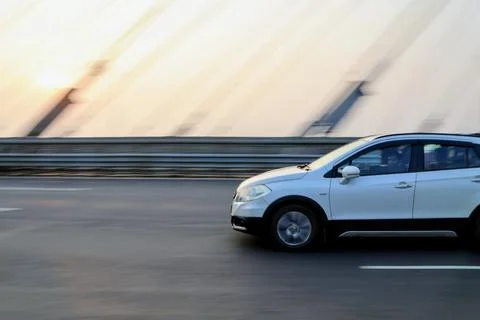 Side view of a vibrant red hatchback driving fast on a city highway bridge Stock Photos