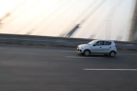 Side view of a vibrant red hatchback driving fast on a city highway bridge Stock Photos