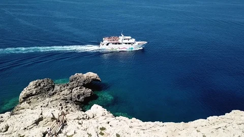 Side view on a white boat sailing on the blue sea along the cliff, Cyprus Stock Footage