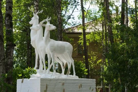 Side view of white deer sculptural group against shaded foliage in Ukhta Stock Photos