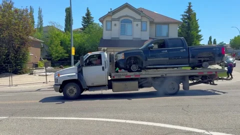 Side view of a white flatbed tow truck transporting a black wheel-less pickup Stock Footage 337682484