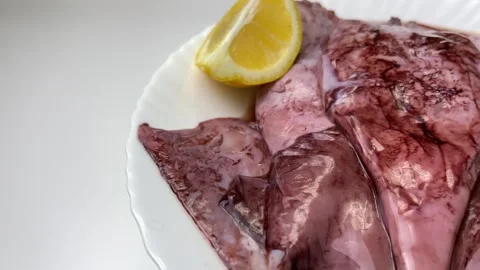 Side view on a white plate there are unpeeled raw squid and lemon slices on a Stock Footage 320537116