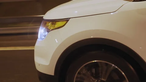 Side view of white SUV car front riding on wet asphalt road, headlight shining Stock Footage 195929655