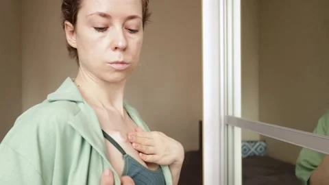 Side view of a woman adjusting an open shirt near her chemotherapy port at .. Video stock 336071649