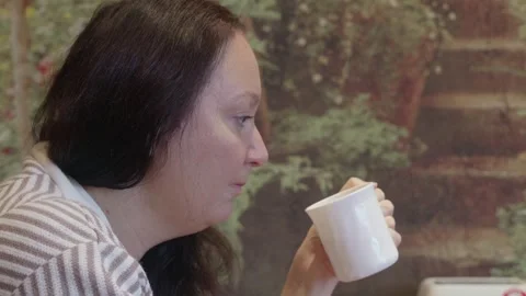 Side view woman drinking tea from white mug near window with striped cardigan Video stock 320263184