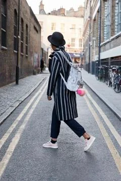 Side view of woman in hat and striped coat walking in street Stock Photos