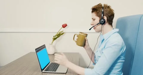 Side View of Woman Talking on Headset and Using Laptop at Desk  Drinking Coffee Stock Footage 288238561