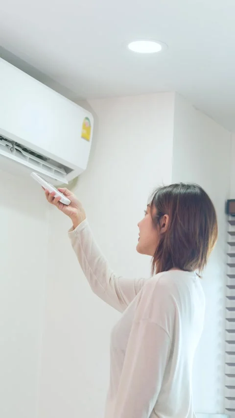 Side View of Woman Using Remote Control to Adjust Air Conditioner Stock Footage 342131660