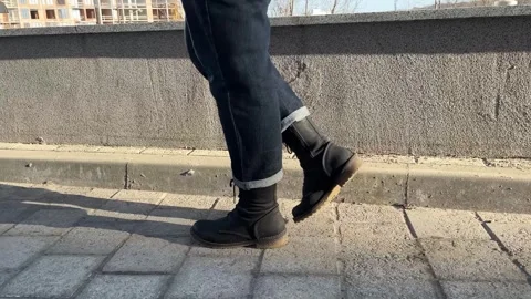 Side View of Woman Walking in Black Boots and Dark Jeans on Sunlit Sidewalk Stock Footage 330801880