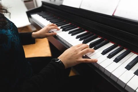 Side view of woman's hands playing piano by reading sheet music. Selective focus Stock Photos