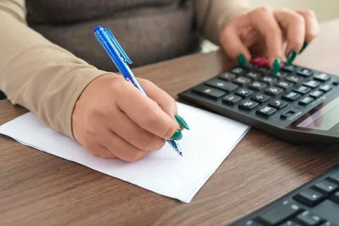 Side view of woman's hands. She is using her calculator and writing numbers down Stock Photos