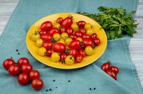 Side view of yellow and red tomatoes in plate and green mint leaves on blue.. Stock Photos
