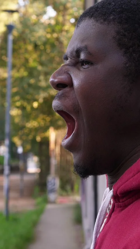 Side view of young African man yawning while standing in urban park 動画素材 335696442