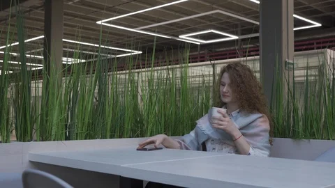 Side view of a young and pretty woman with red hair who is sitting in a cafe Stock Footage 102346137