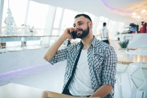 Side view of young bearded man,dressed incasual wear,sitting at round wooden Stock-Fotos