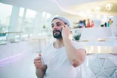 Side view of young bearded man,dressed in gray cardigan,sitting at round wooden Stockfoto's