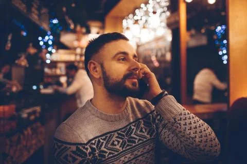 Side view of young bearded man,dressed incasual wear,sitting at round wooden Stockfoto's