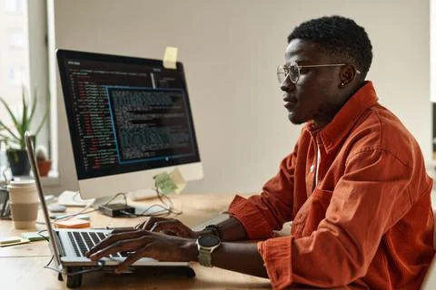 Side view of young black man in smart casualwear and eyeglasses decoding data Stock Photos