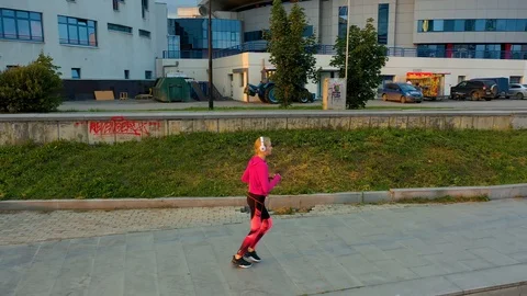 Side view of young blonde in white headphones woman running along pond Stock Footage 115084889