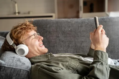 Side view young british ginger man in headphone talking on video call via phone Stock Photos