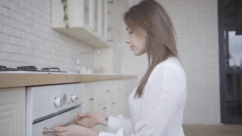 Side view of young brunette Caucasian woman opening oven and looking inside Video stock 126436809