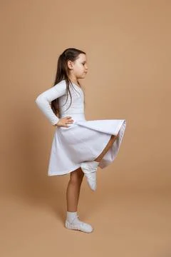 Side view of young cute serious girl with long dark hair in white dress, socks Stock Photos