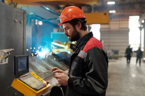 Side view of young engineer in workwear using digital tablet Stock Photos