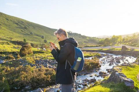 Side view young explorer man trekking in mountains, using mobile phone for GPS Stock Photos